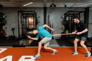 Coach guiding athlete in resistance band exercises for strength and endurance indoors.