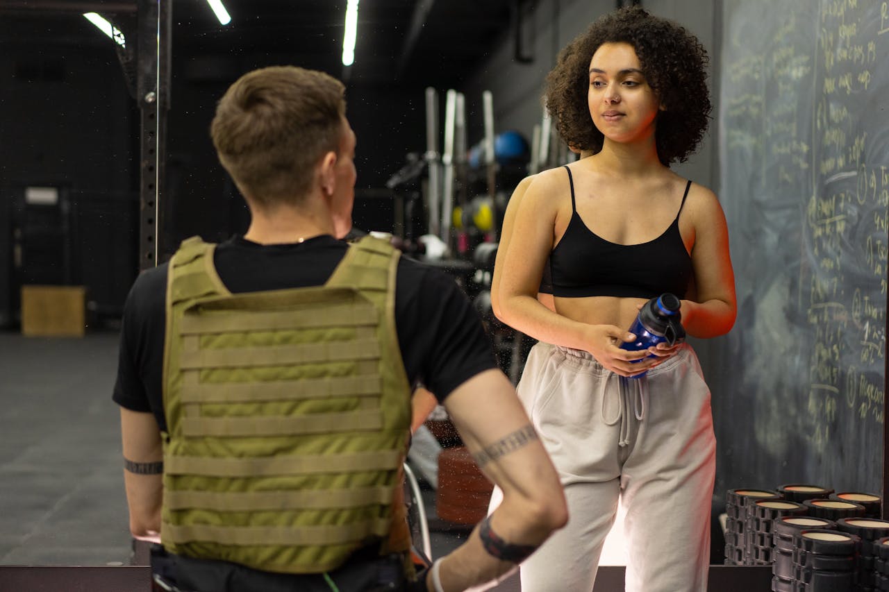 A personal trainer and client engage in conversation at a gym, highlighting fitness and training concepts.